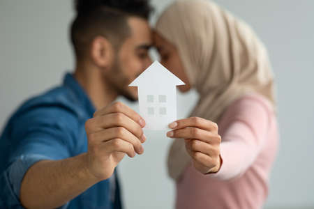 Young loving muslim couple middle eastern man and woman in hijab showing paper house at camera and touching each other with foreheads, real estate and relocation concept, copy spaceの写真素材