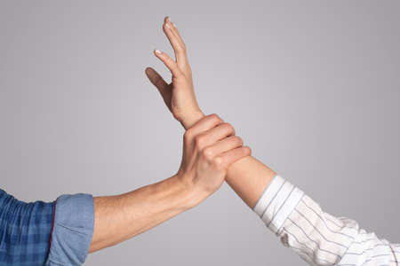 Social violence, issue, fighting and harassment at home during covid-19. Millennial male hand holding female arm, isolated on gray background,の写真素材