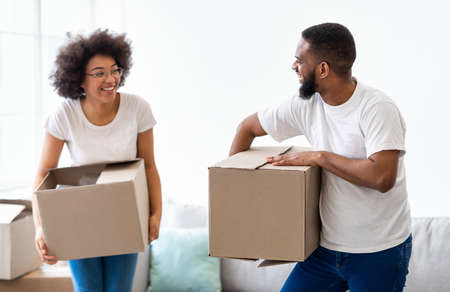 Relocation. Joyful African Couple Laughing Carrying Moving Boxes Together Entering New Home. Real...