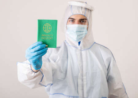 Medical specialist in protective biohazard costume showing virus immunity passport on light studio background, selective focus.の写真素材