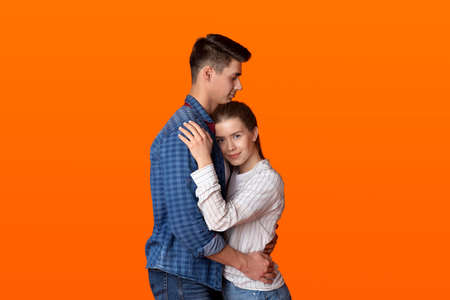 Happy date, emotions of love, relationship in free time during lockdown. Calm young attractive man and woman hugging, isolated on orange background, studio shot, cut out, copy spaceの写真素材