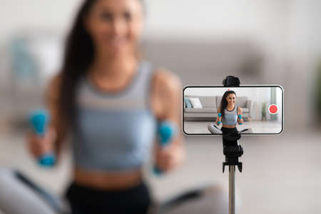 Selective focus on mobile phone screen shooting young woman fitness trainer, active sporty lady...