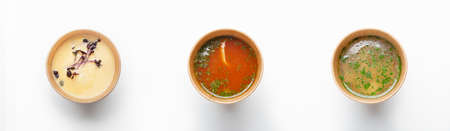 Healthy food, modern restaurant menu, tasty, yummy meal. Fresh appetizing soups assortment with baby spinach and herbs in paper eco cups, isolated on white background, top view, panorama, copy spaceの写真素材