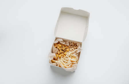 Delicious snacks for beer for group of people and modern delivery at home, ad of food services. Tasty peanuts, corn, cheese in paper box, isolated on white background, top view, flat lay, copy spaceの写真素材