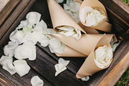 Congratulations to newlyweds and wedding accessories on ceremony. White rose petals in paper packages in wooden box for showering bride and groom at marriage , top view, flat lay, free space, close upの写真素材
