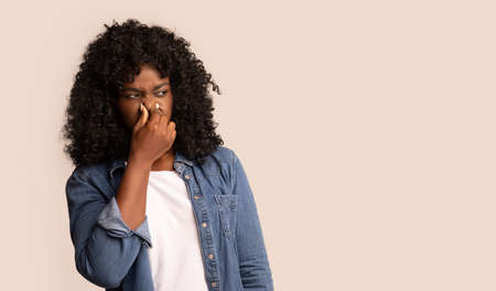 Portrait of black woman closing nose with fingers, feeling unpleasant scent, african american lady...