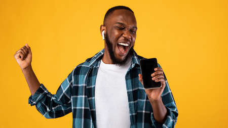 Mobile Karaoke Application. African Guy Singing Holding Phone Like Microphone Having Fun Listening...