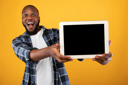 Great Application. Excited Black Guy Showing Tablet Computer With Empty Screen To Camera Recommending New App Posing Standing Over Yellow Studio Background. Digital Tablet Display Mockup For Advertの写真素材