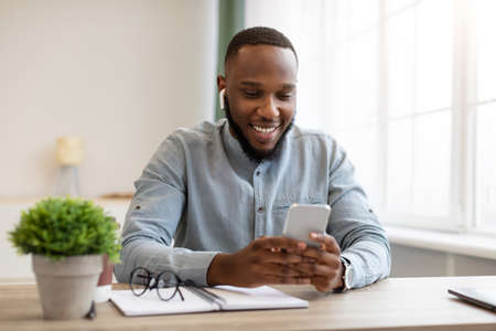 Business Application. Happy Black Businessman Using Smartphone And Earbuds Listening To Business...