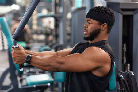 Side view of black guy bodybuilder making work out for shoulders and chest muscles at gym, copy...