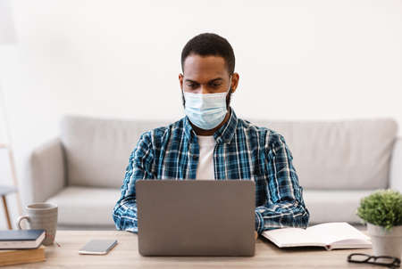 Black Businessman At Laptop Wearing Face Mask Working On Computer Online Sitting In Modern Office.
