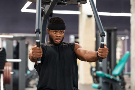 Young black sportsman training shoulders muscles and chest on block exerciser in gym, copy space. Motivated african american bodybuilder having workout at modern gym, using peck deck machineの写真素材
