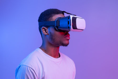 Portrait Of Young Black Man In VR Headset Standing In Neon Light Over Purple Background, Calm African American Guy Playing Video Game, Enjoying Virtual Reality Experience, Closeup With Free Spaceの写真素材
