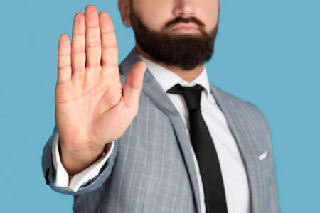 Cropped view of millennial businessman refusing something, showing STOP gesture on blue studio...