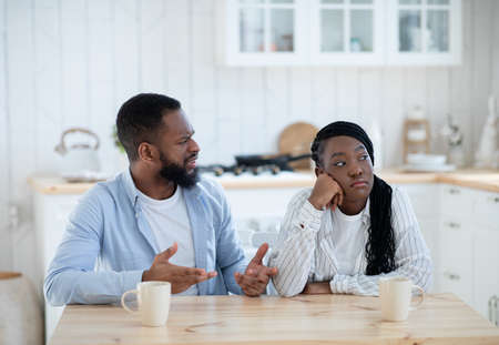 Marriage Crisis. Upset Black Woman Listening Complaints From Husband In Kitchen At Home, Young African American Man Blaming Wife For Problems In Relationship, Suffering Misunderstanding, Copy Spaceの写真素材