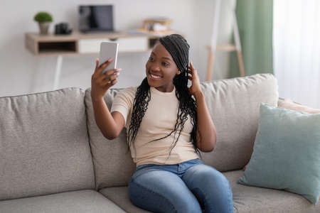 Cute young black lady with stylish dreadlocks taking selfie on smartphone for social media or...