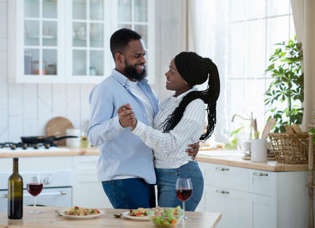 Romantic Moments. Young Happy Black Couple Dancing Together In Kitchen, Affectionate African American Lovers Having Fun While Spending Time At Home, Eating Tasty Food And Drinking Red Wineの写真素材