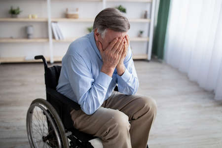 Depression in older adults with disability. Unhappy senior man in wheelchair crying from loneliness at home. Physically impaired male patient suffering from emotional problemsの写真素材
