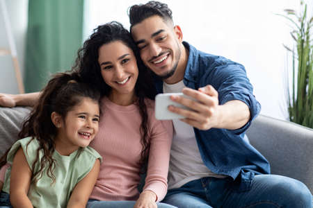 Arab Man Taking Selfie On Smartphone With Wife And Daughter At Homeの写真素材