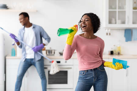 Black lady having fun with her boyfriend while cleaning kitchen