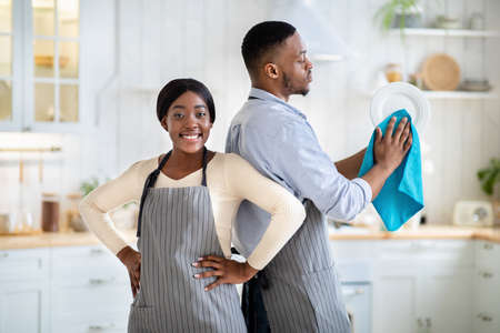 Portrait of positive black woman and her husband wiping dishes at kitchenの写真素材
