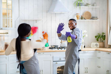 Cheerful black couple having mock fight with cleaning detergents at kitchenの写真素材