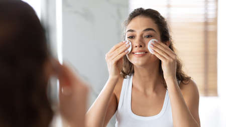 Woman Moisturizing Skin Removing Makeup With Cotton Pads In Bathroomの写真素材