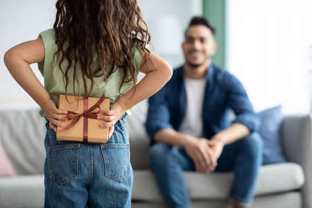 Little girl greeting her dad with Fathers Day, holding gift behing backの写真素材