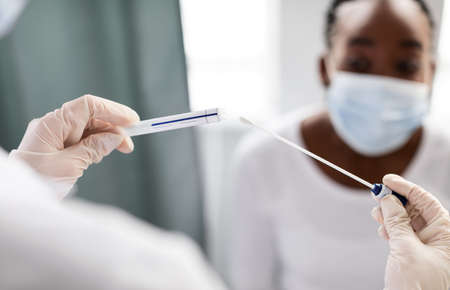 Doctor taking PCR test sample from potentially infected afro womanの写真素材