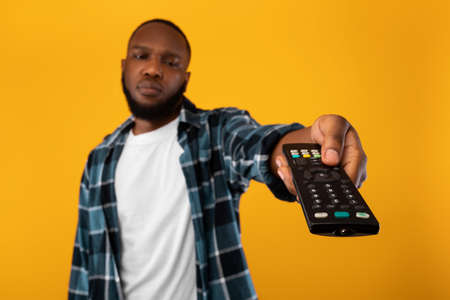 Bored African Man Switching Channels Pointing Television Controller, Yellow Backgroundの写真素材