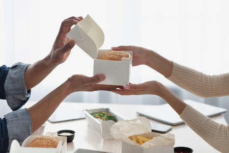 Millennial african american man opens box with burger for lady with fast foodの写真素材