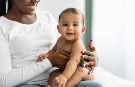 Cute little African American infant sitting on bed with mother