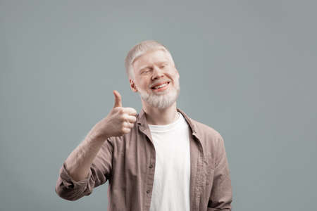Happy albino guy showing thumb up gesture, approving or recommending something good, posing over grey backgroundの写真素材