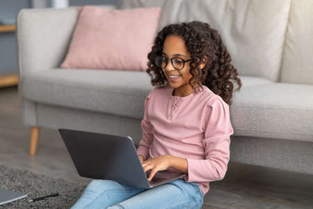 E-learning concept. African american gen z girl using her laptop, doing homework, watching online...
