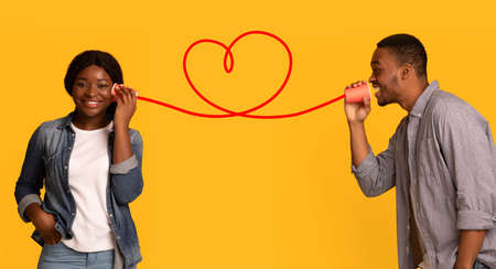 Affectionate black guy whisperinf words of love to girlfriend via tin phoneの写真素材