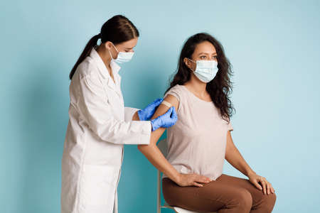 Female Getting Vaccinated, Nurse Applying Plaster On Arm, Blue Backgroundの写真素材