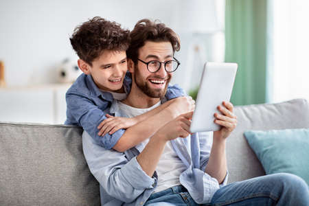 Modern technologies for leisure. Happy father and son using digital tablet, searching film together at homeの写真素材