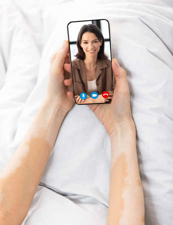 Woman making video chat with friend while lying in bed with smartphoneの写真素材