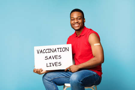 African Man Holding Board Advertising Covid-19 Vaccination Over Blue Backgroundの写真素材