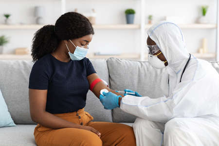 Doctor in protective suit taking blood sample for female patientの写真素材