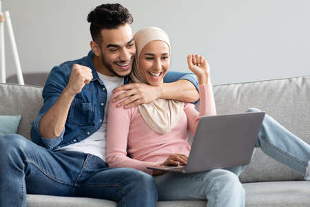 Happy arab couple with laptop raising fists upの写真素材
