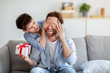 Happy fathers day. Son congratulating his daddy, covering his eyes from behind and giving present at homeの写真素材
