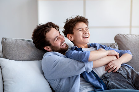 Family weekend. Loving dad tickling his laughing son, spending leisure time at home togetherの写真素材