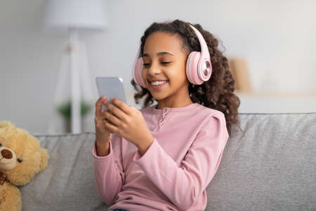 Leisure concept. Happy girl listening to music in wireless headphones, chatting on her smartphoneの写真素材