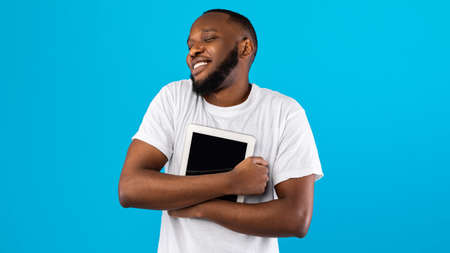 African American Guy Hugging Digital Tablet Over Blue Background, Panoramaの写真素材