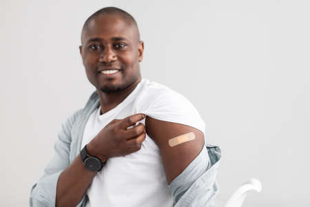 Happy black man showing the bandage after coronavirus vaccine shot