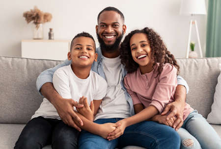 African american father hugging his children sitting on couchの写真素材