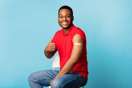 Happy Vaccinated African American Guy Gesturing Thumbs-Up Over Blue Backgroundの写真素材
