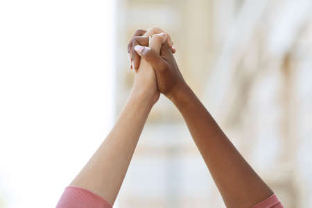 Unrecognizable black and caucasian ladies holding handsの写真素材