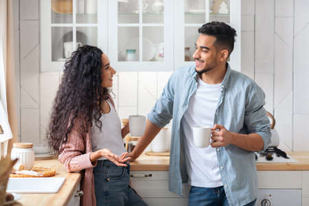 Cheerful Middle Eastern Couple Relaxing In Kitchen Together, Drinking Coffee And Chattingの写真素材